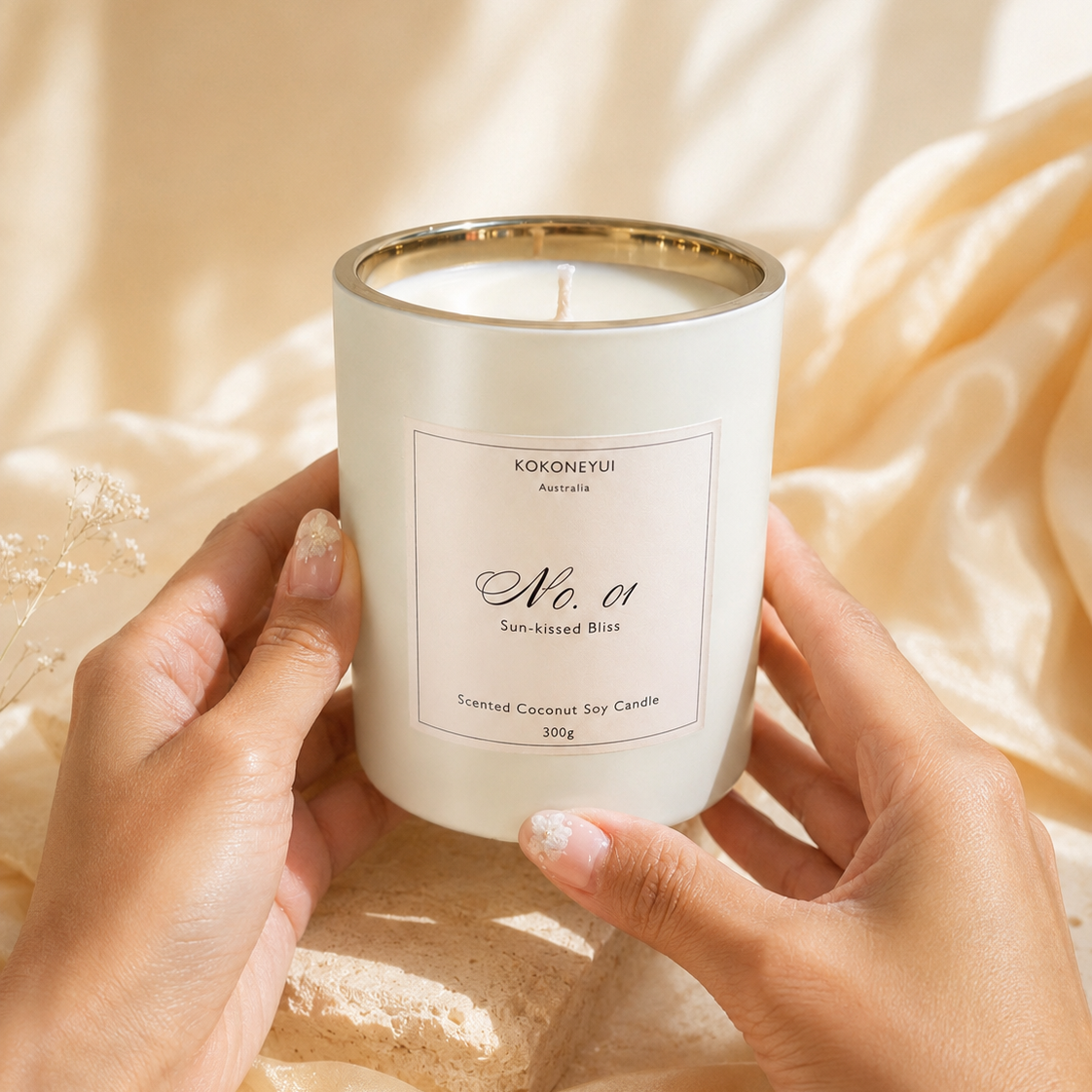 Candle with a label held by hands against a soft, beige fabric background
