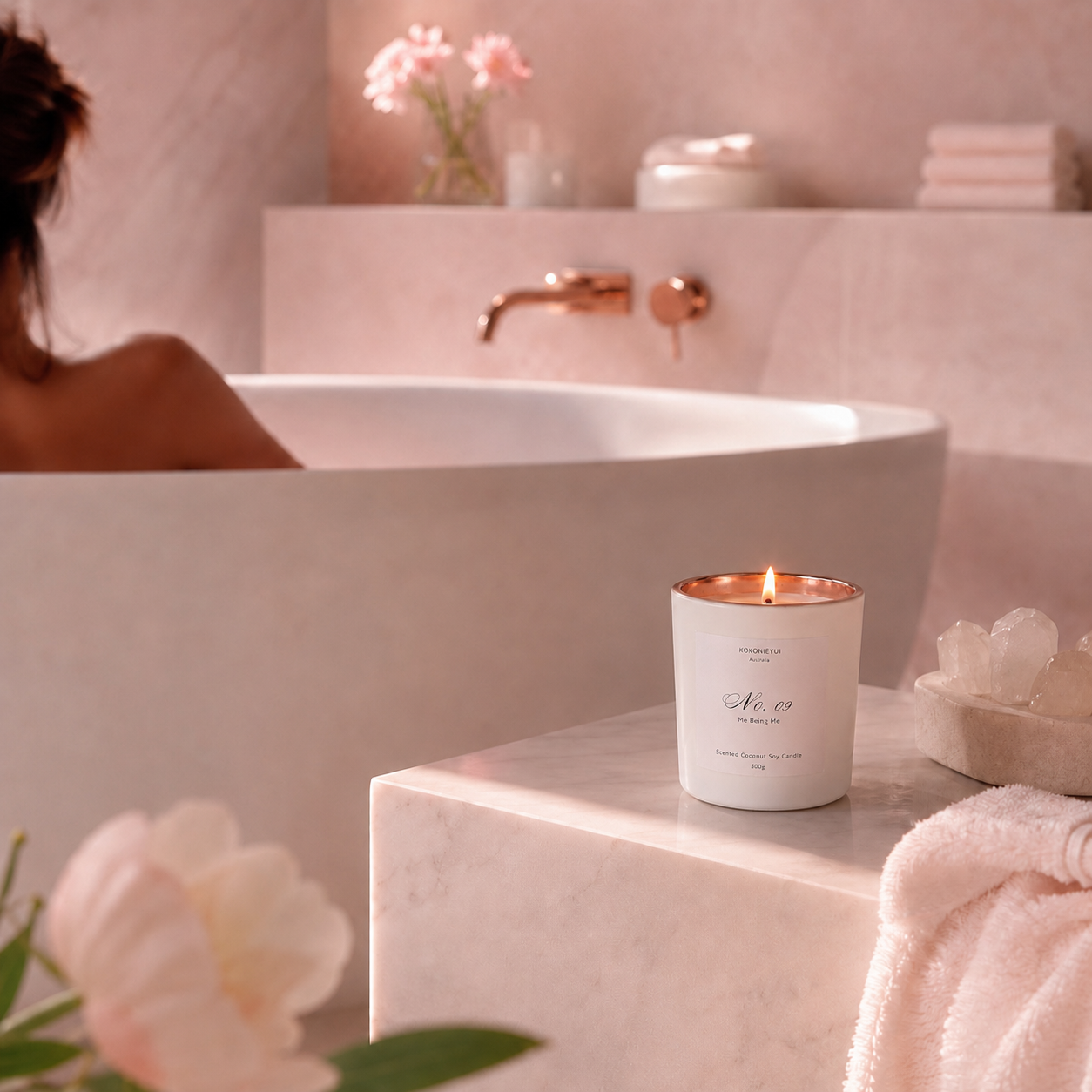 Candle on a bathroom counter with a bathtub and flowers in the background