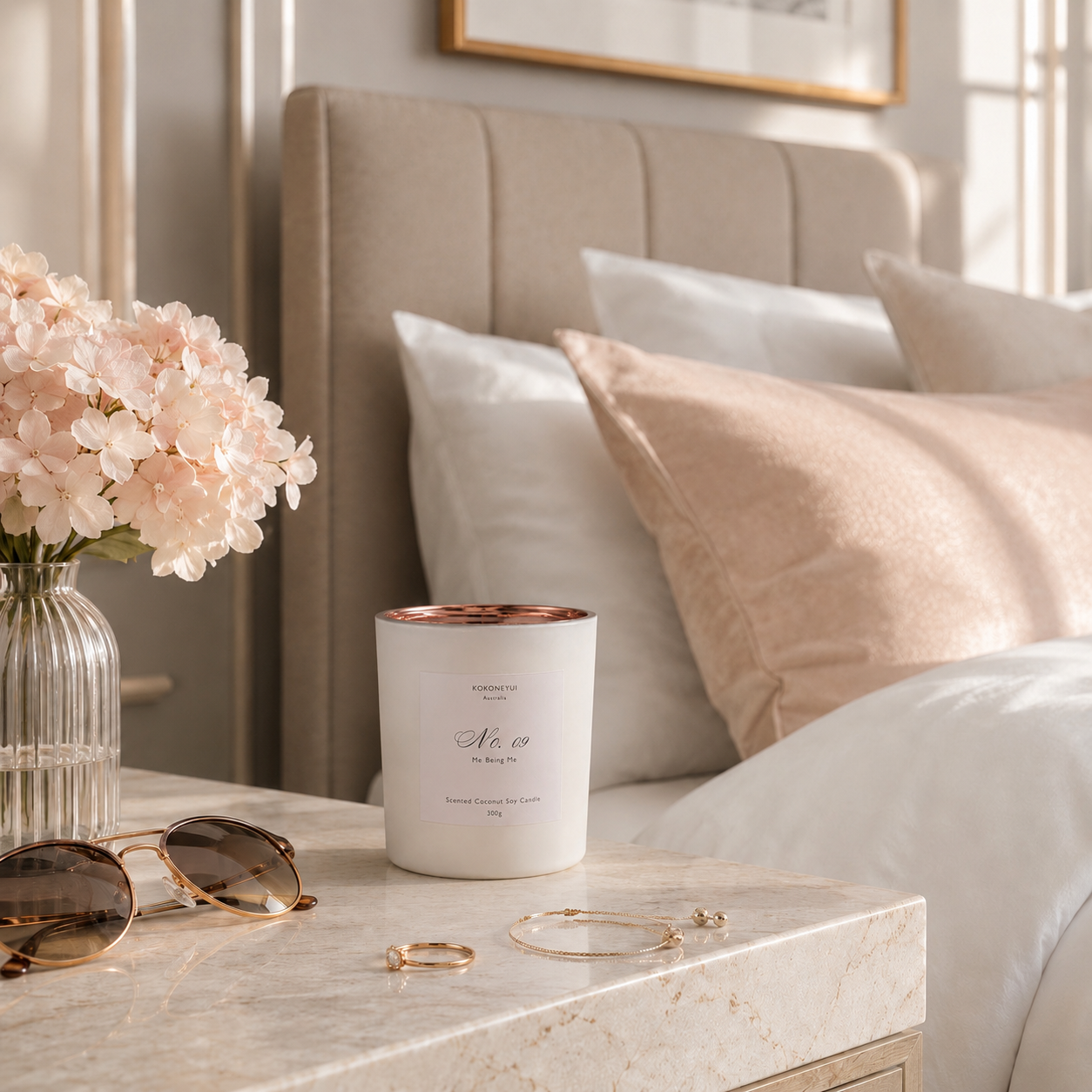 Candle, sunglasses, and jewelry on a nightstand with a bed in the background