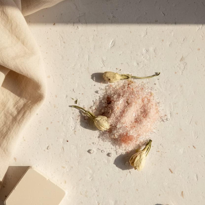 Pink salt crystal with dried flowers on a textured white surface