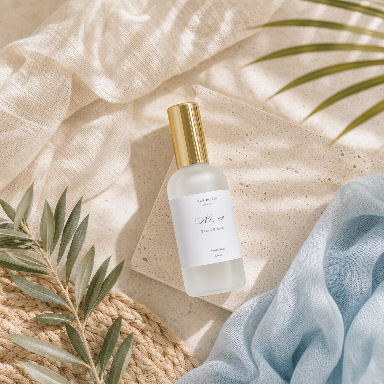 Room mist bottle with gold cap on a textured beige surface with green leaves
