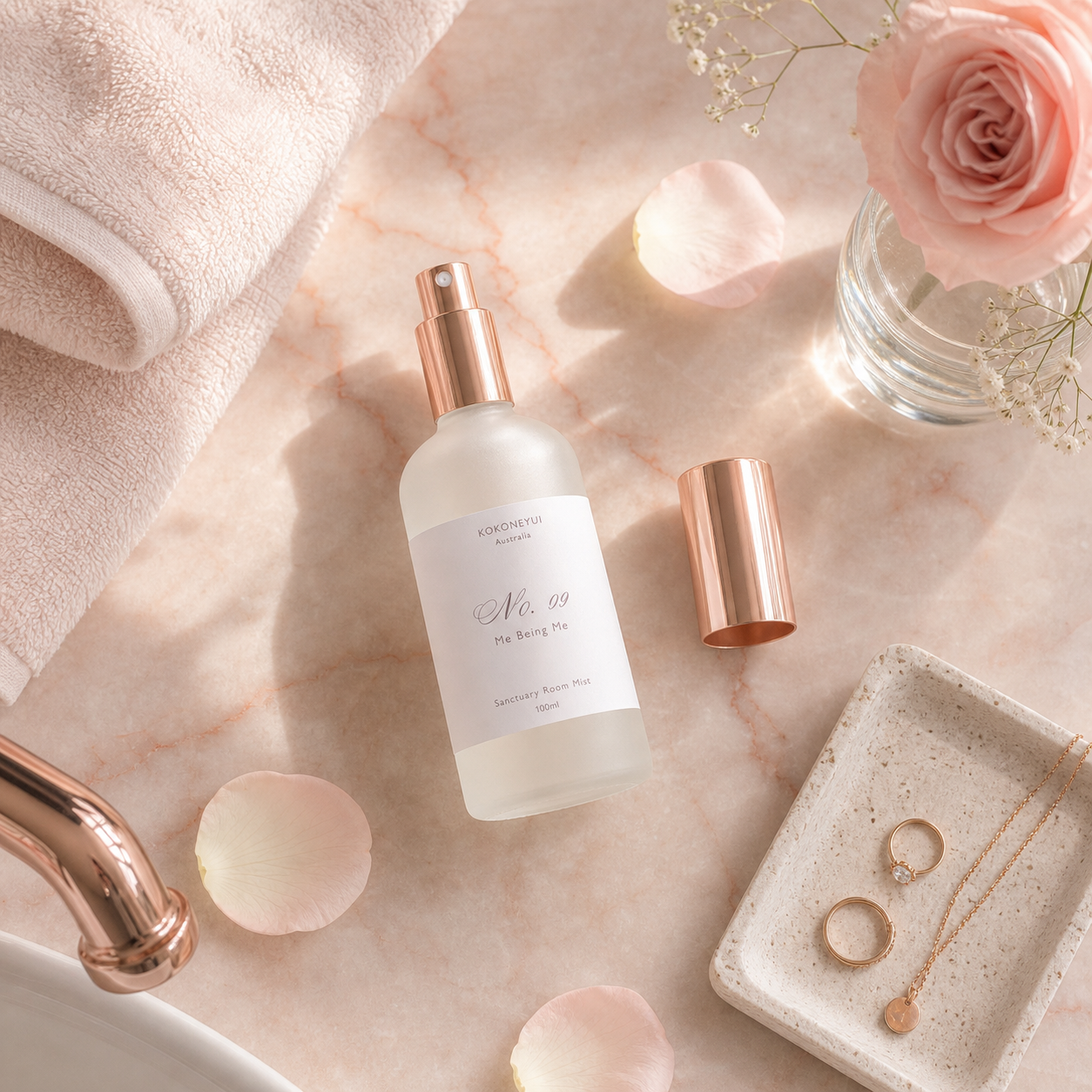 Room Mist bottle with rose gold cap on a marble surface with flowers and jewelry