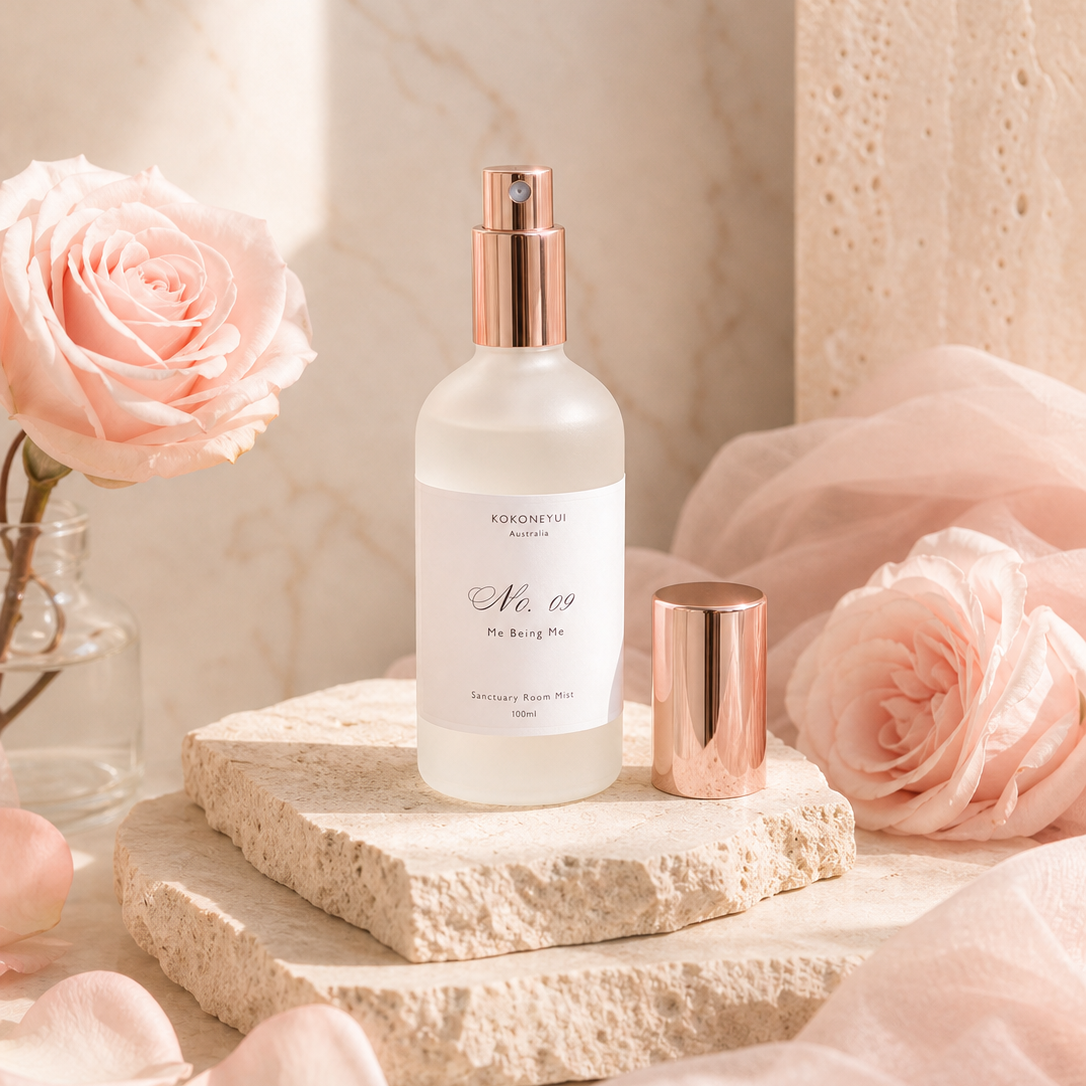 Room Mist Bottle with rose gold cap on a marble surface with pink roses in the background