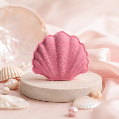 Pink shell-shaped bath bomb on a beige stand with seashells and pearls on a soft pink background