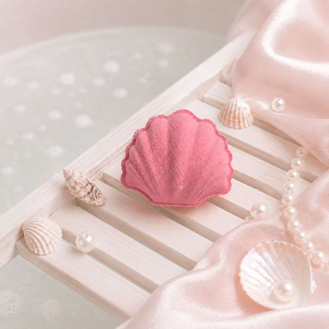 Pink shell-shaped bath bomb on a white surface with pearls and seashells.