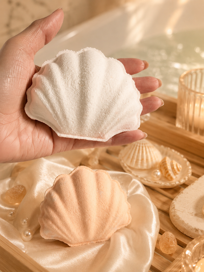 Shell-shaped bath bombs held in a hand with a bathtub and shells in the background