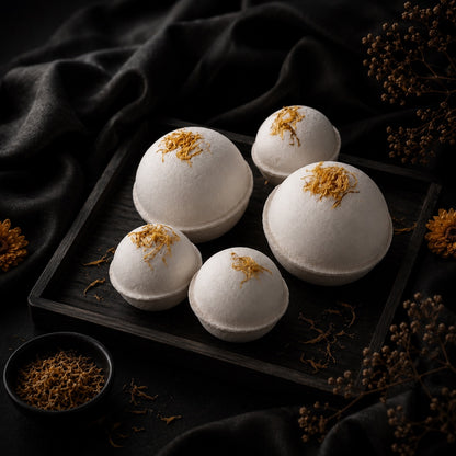 White bath bombs with gold flakes on a dark tray with dark fabric and dried flowers in the background