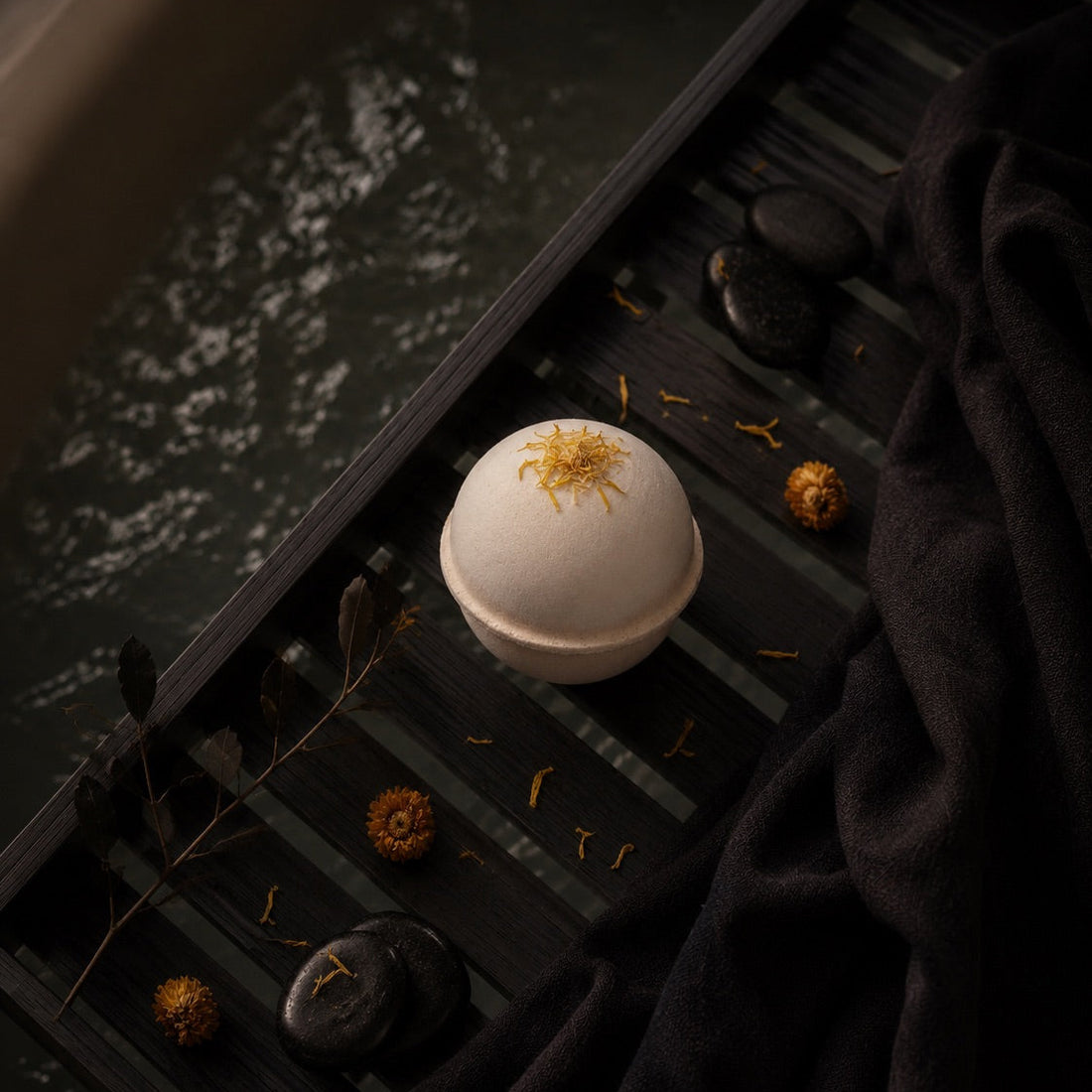 Bath bomb with Calendula flower petals on a dark surface with water reflection