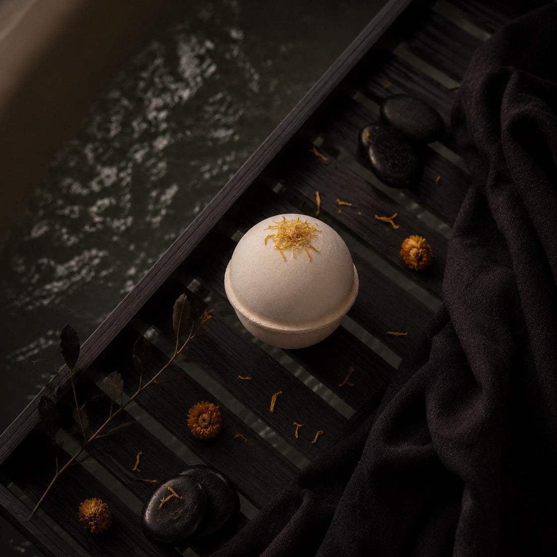 Bath bomb with Calendula flower petals on a dark surface with water reflection