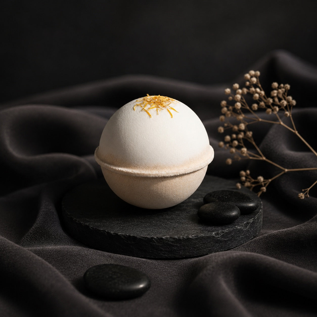 Bath bomb with decorative top on a black surface with stones and dried plants