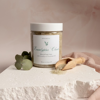 Jar of Eucalyptus Clear bath salts with a wooden scoop on a white stone surface.