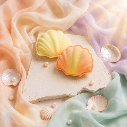 Shell-shaped bath bombs on a stone surface with pearls and colorful fabric in the background