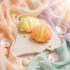 Shell-shaped bath bombs on a stone surface with pearls and colorful fabric in the background