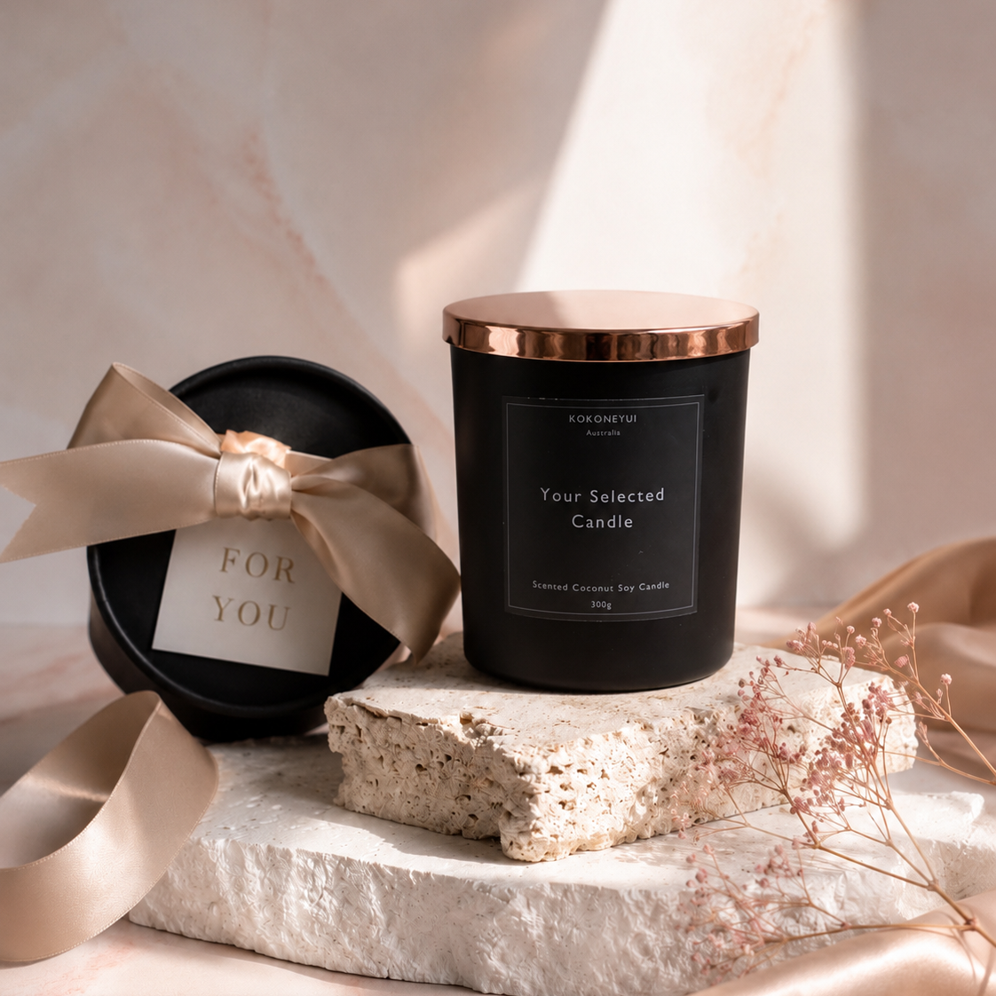 Black candle with a rose gold lid on a marble surface, accompanied by a decorative box and ribbon.