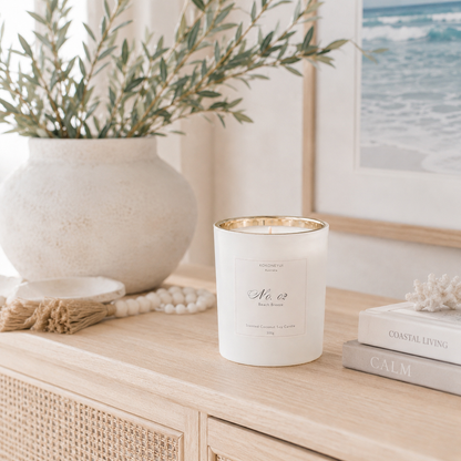 White candle with gold rim on a wooden surface next to a plant and books.