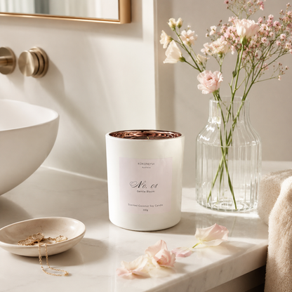 White candle with rose gold lid on a bathroom counter next to a vase of flowers