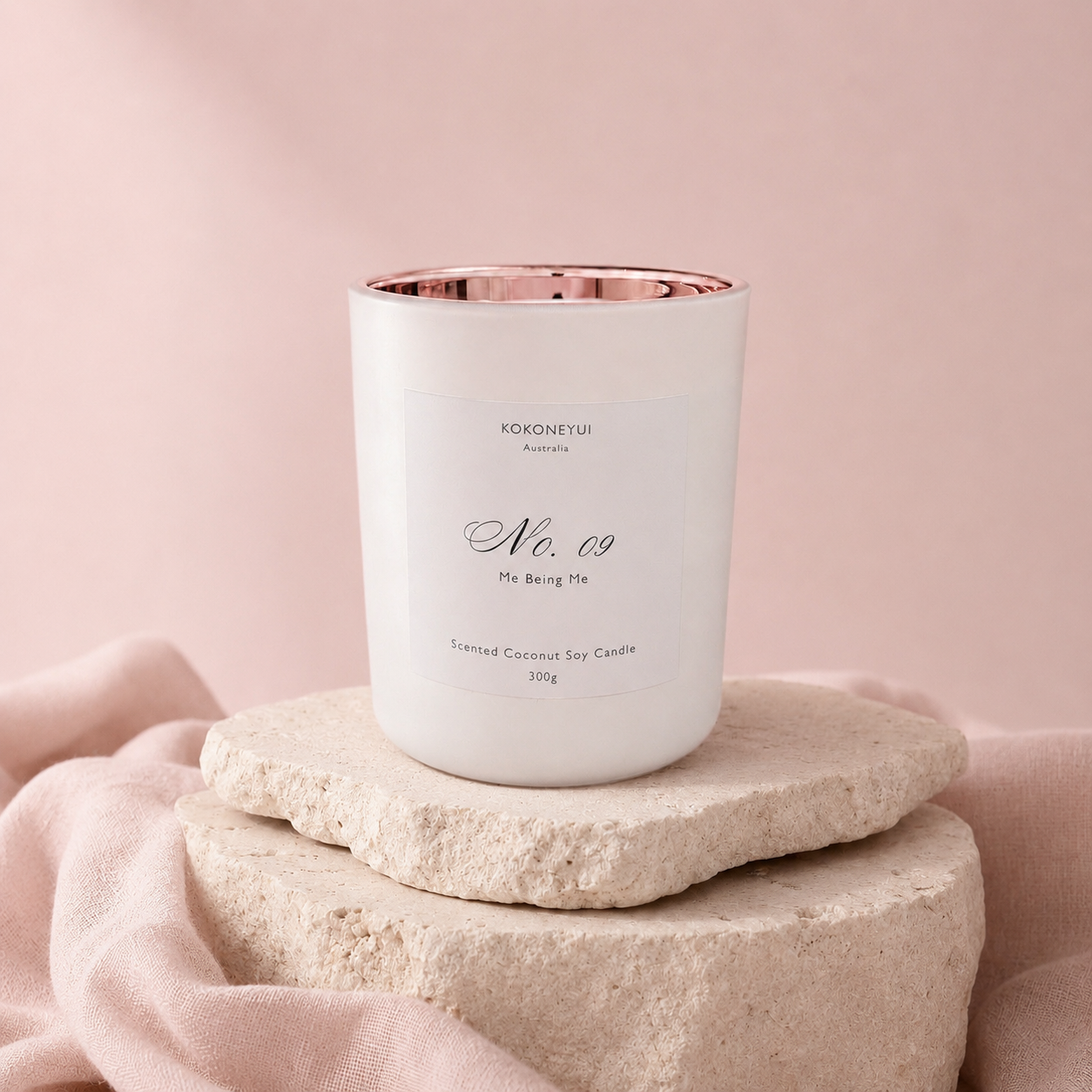 Candle with a rose gold interior on a stone platform against a pink background