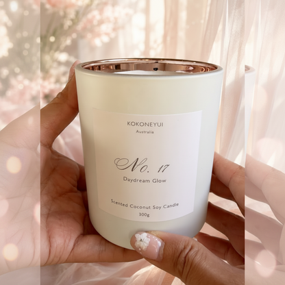 Hand holding a white candle with a gold lid labeled &