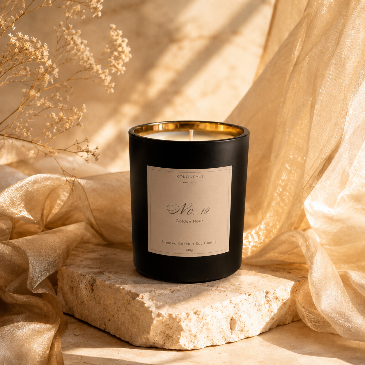 Candle with ivory label on a stone surface with beige fabric and flowers in the background