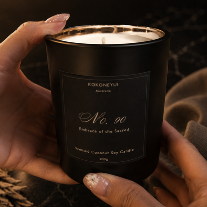 Black candle with a label held by hands against a dark background