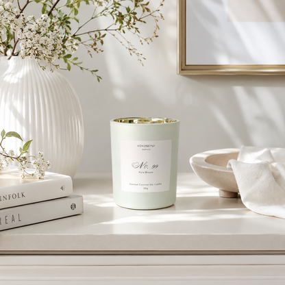 Candle with a white label on a surface with books, a vase, and flowers in the background