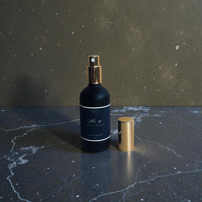 Black spray bottle with gold nozzle on a dark marble surface