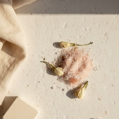 Pink salt crystal with dried flowers on a textured white surface
