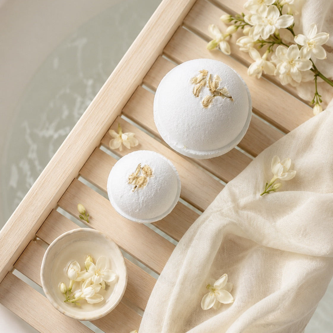 Bath bombs with flowers on a wooden tray over a bathtub.