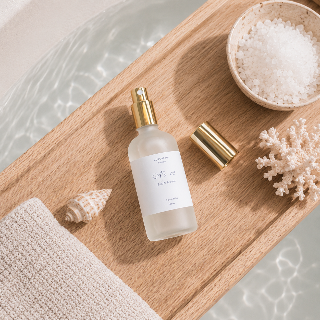 Room mist bottle with gold cap on a wooden tray with sea salt, shell, and coral.