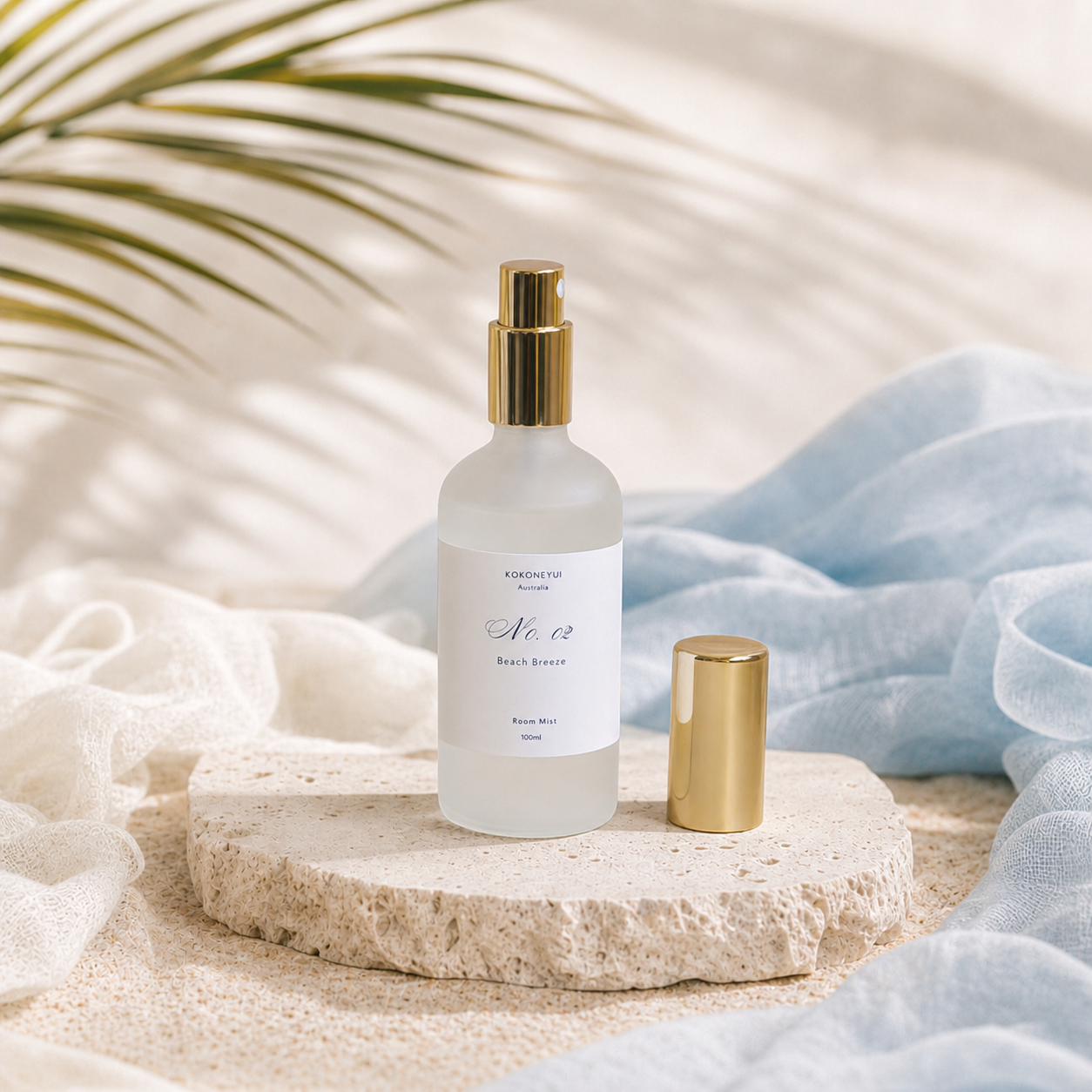 Room mist bottle with gold cap on a stone surface with soft fabric and plant leaves in the background
