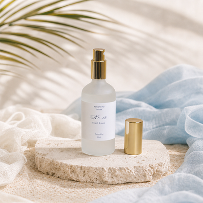 Room mist bottle with gold cap on a stone surface with soft fabric and plant leaves in the background
