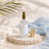 Room mist bottle with gold cap on a stone surface with soft fabric and plant leaves in the background