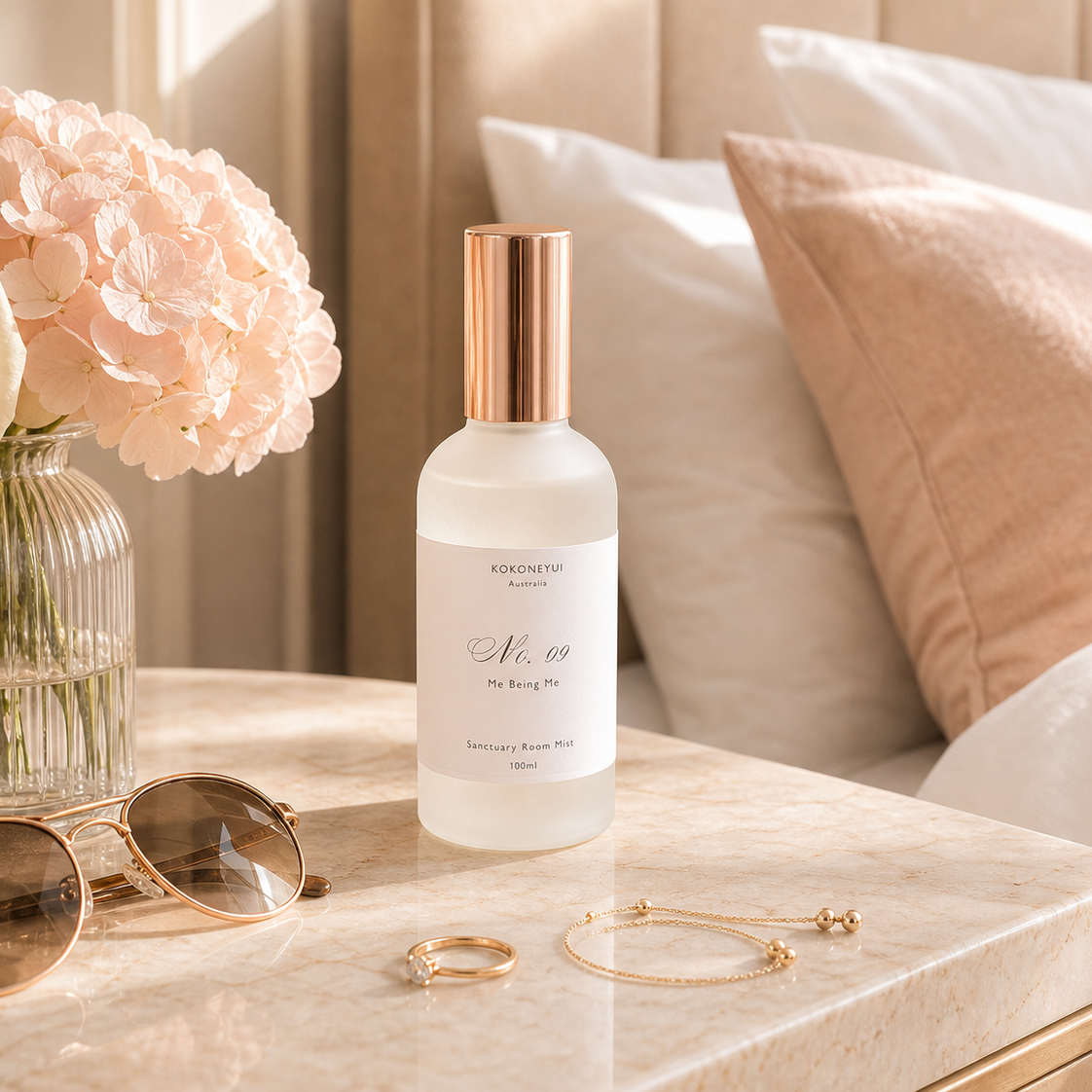 Room Mist Bottle on a marble surface with flowers, sunglasses, and jewellery in the background.
