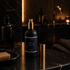 Black spray bottle with gold cap on a dark marble surface in a bathroom setting