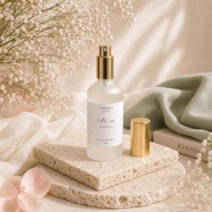 Room mist bottle with gold cap on a stone surface with flowers and fabric in the background