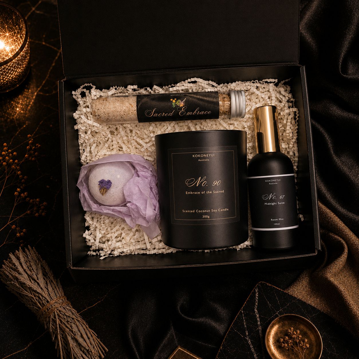 A curated gift set in an open black box, featuring a black candle labeled &