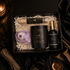 A curated gift set in an open black box, featuring a black candle labeled &